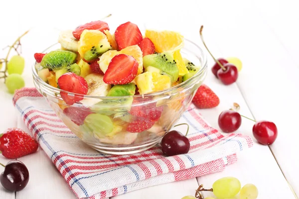 Glass bowl with fresh fruits salad and berries on white wooden table — 图库照片
