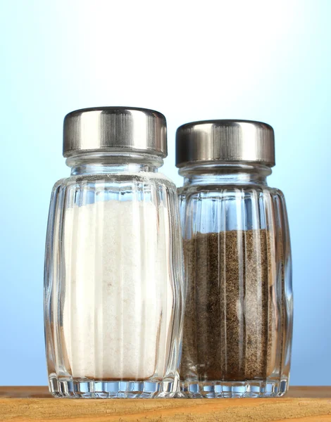 Sól i pieprz mills, na drewnianym stole na niebieskim tle — Zdjęcie stockowe