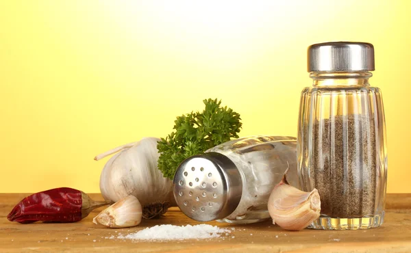 Salt and pepper mills, garlic and parsley on wooden table on yellow background — Stock Photo, Image