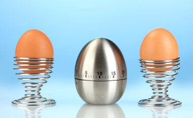 Egg timer and egg in metal stand on blue background clipart