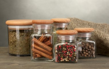 Jars with spices on wooden table on grey background clipart