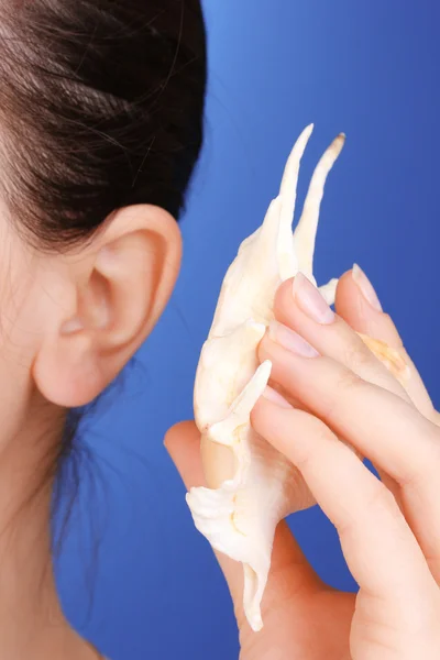 Human ear and shell close-up on blue background — Stock Photo, Image