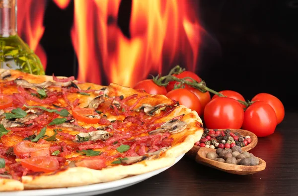 Heerlijke pizza en tomaten op houten tafel op vlam achtergrond — Stockfoto
