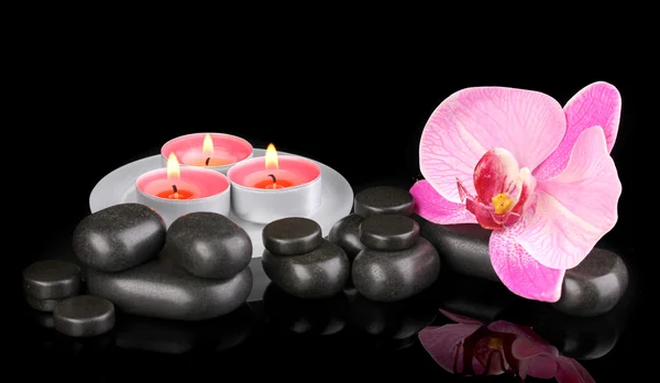 Pietre termali con fiore di orchidea e candele isolate su nero — Foto Stock