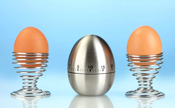 Χρονόμετρο αυγό και το αυγό σε μέταλλο σταθεί σε μπλε φόντο — Φωτογραφία Αρχείου