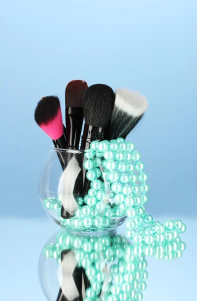Pincéis de maquiagem em uma tigela com colar de pérolas no fundo azul — Fotografia de Stock