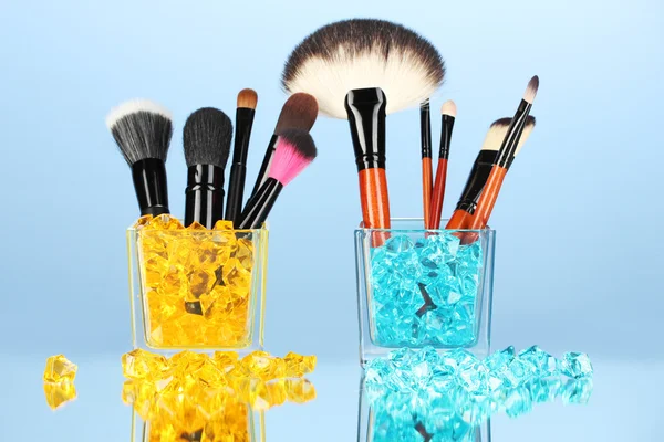 Make-up brushes in two glass cup with stones on blue background — Stock Photo, Image