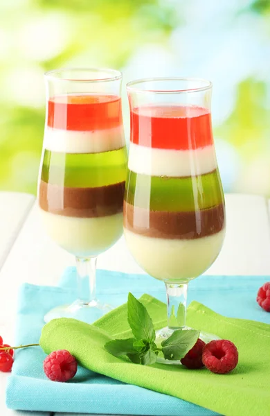 Fruit jelly in glasses, berries and mint on wooden table on green background — Stock Photo, Image