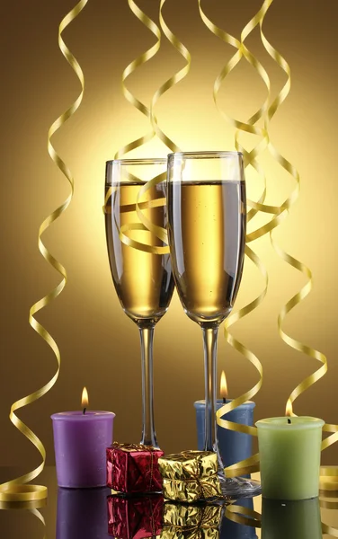 Glasses of champagne, candles, gifts and streamer on yellow background — Stock Photo, Image