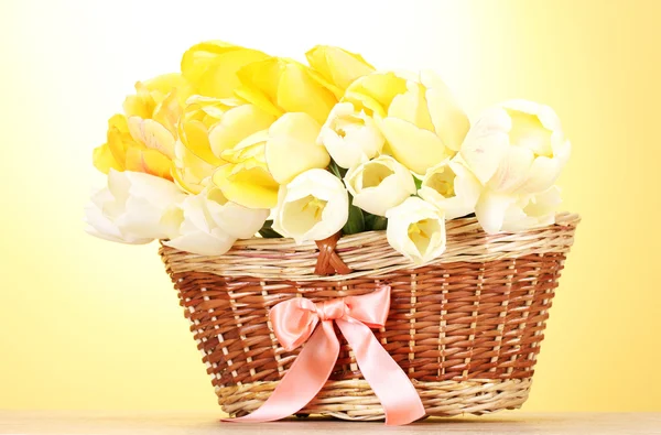 Piękne tulipany w kosz na drewnianym stole na żółtym tle — Zdjęcie stockowe