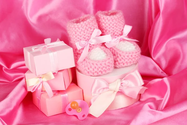 Růžové dětské boty, dudlík, dary na hedvábné pozadí — Stock fotografie