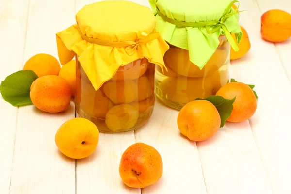 Canned apricots in a jars and ripe apricots on white wooden table — Stock Photo, Image