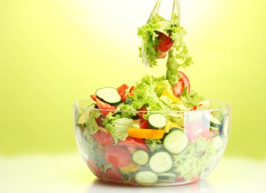 Fresh vegetable salad in transparent bowl with spoon and fork on green background clipart