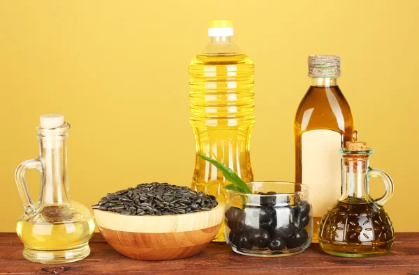 Azeite e óleo de girassol nas garrafas e pequenos decantadores em fundo amarelo close-up — Fotografia de Stock