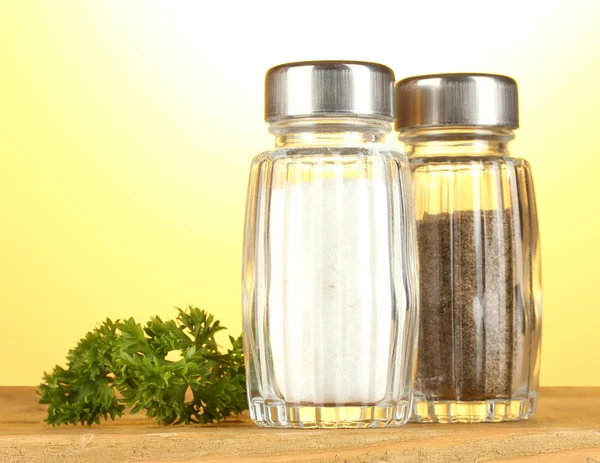 stock image Salt and pepper mills and parsley on wooden table on yellow background