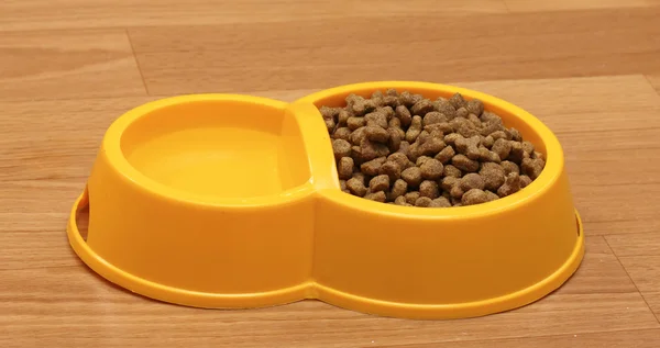 Comida de gato seco e água em tigela amarela no chão — Fotografia de Stock