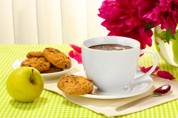 Kubek gorącej czekolady, jabłko, ciasteczka i kwiaty na stole w kawiarni — Zdjęcie stockowe