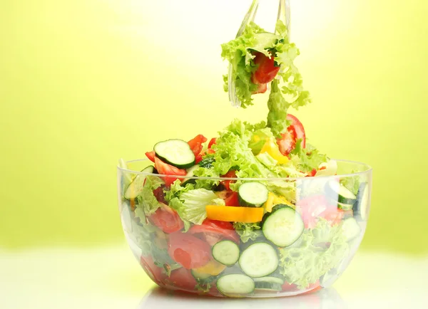 Ensalada de verduras frescas en un tazón transparente con cuchara y tenedor sobre fondo verde —  Fotos de Stock