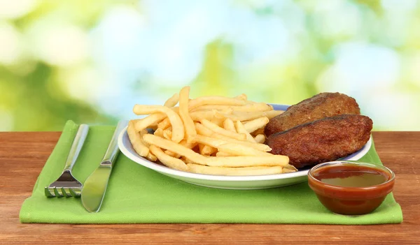 Patate fritte con hamburger sul piatto su sfondo verde primo piano — Foto Stock