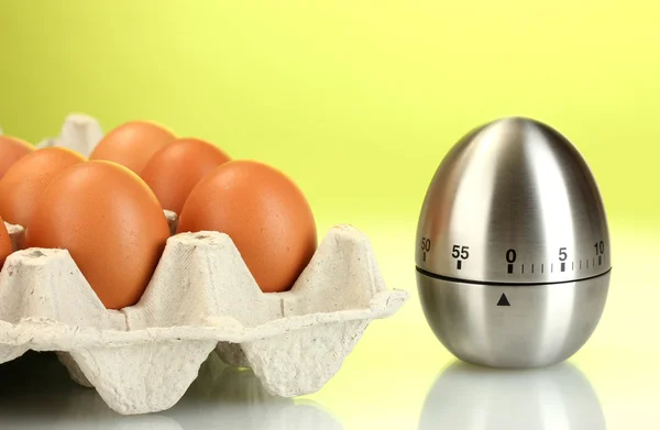 Eier in Schachtel und Eieruhr auf grünem Hintergrund — Stockfoto