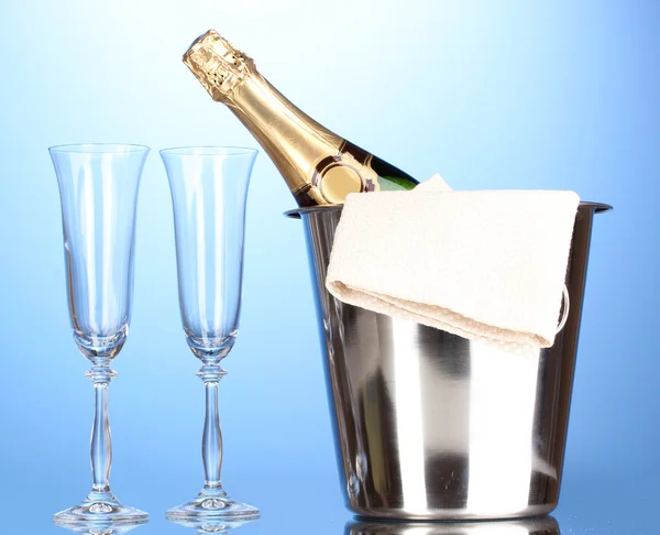 Butelka szampana w wiaderku z lodem i okulary na niebieskim tle — Zdjęcie stockowe