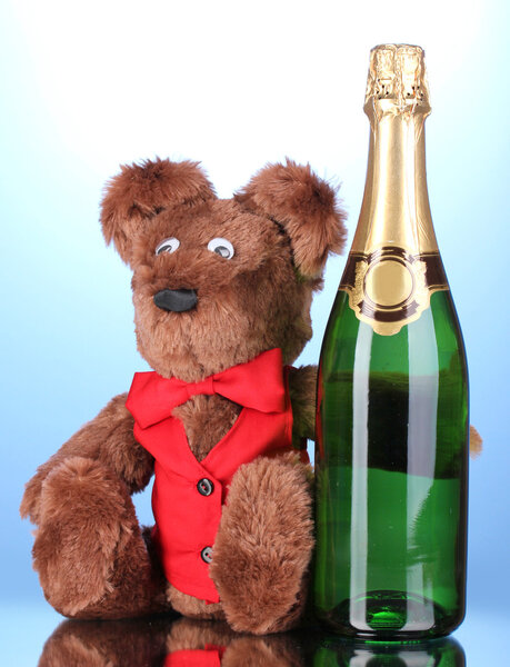 Toy bear and bottle of champagne on blue background