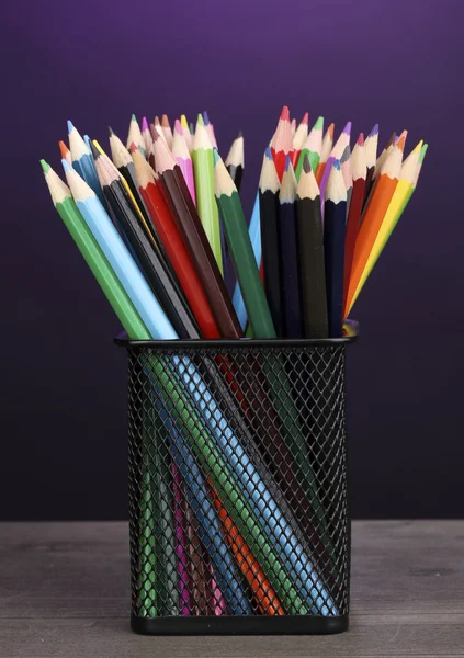 Color pencils in glass on wooden table on violet background — Stock Photo, Image