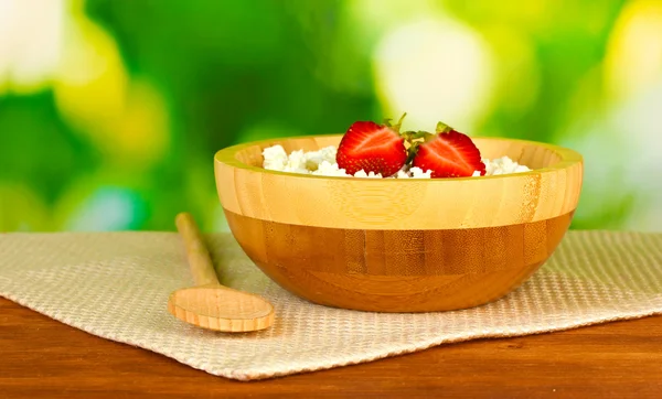 Cottage cheese with strawberry in wooden bowl with wooden spoon on beige napkin on wooden table on green background