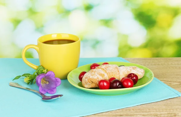 Croissant med körsbär och kaffe på träbord på grön bakgrund — Stockfoto