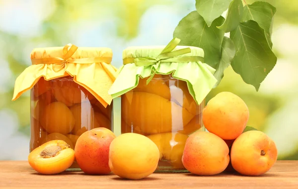 Konzervované meruňky v sklenice a sladké meruňky na dřevěný stůl na zeleném pozadí — Stock fotografie