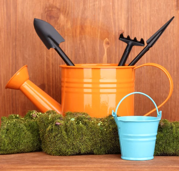Musgo verde e regador com ferramentas de jardinagem em fundo de madeira — Fotografia de Stock