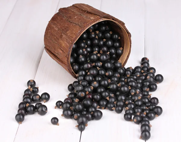 Black currant in wooden cup on wooden background — Stock Photo, Image