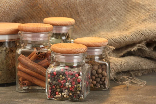 Burkar med kryddor på träbord på säckväv bakgrund — Stockfoto