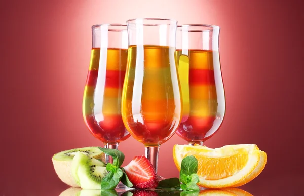 Fruchtgelee in Gläsern und Früchten auf rotem Hintergrund — Stockfoto