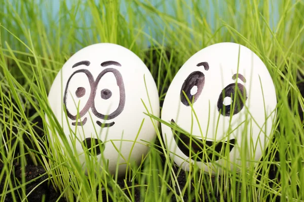 Ovos brancos com rostos engraçados na grama verde — Fotografia de Stock