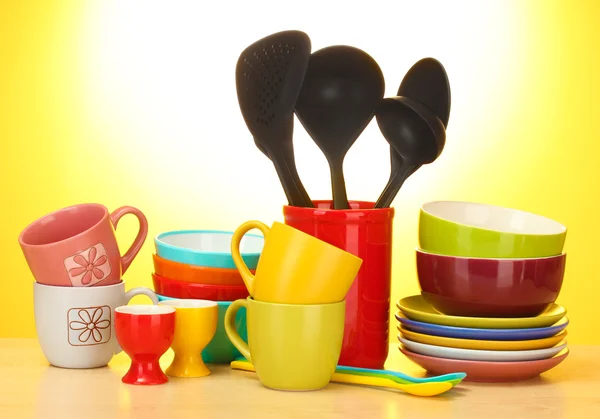 Helle leere Schüsseln, Tassen und Küchenutensilien auf Holztisch auf gelbem Hintergrund — Stockfoto