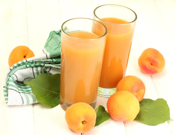 Glasögon av aprikos juice och färska aprikoser på vita träbord — Stockfoto