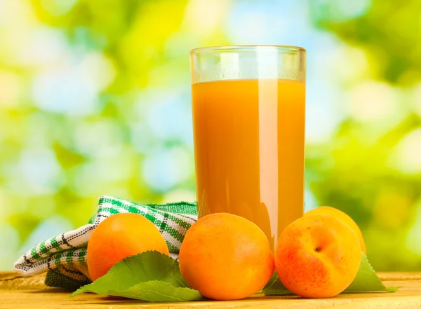 Glass of apricot juice and fresh apricots on wooden table on green background — Stock Photo, Image