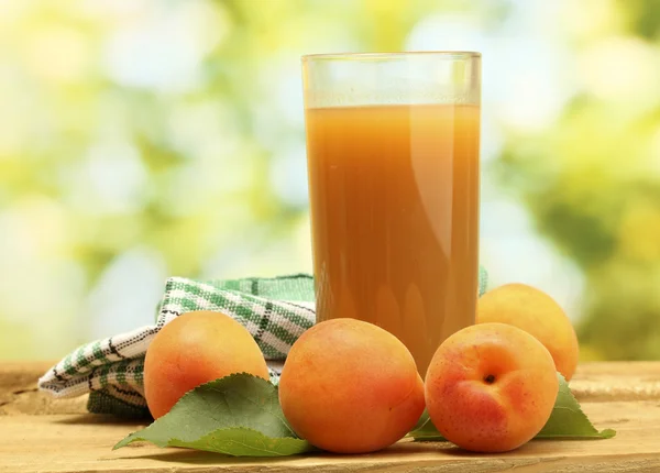 Склянка з абрикосового соку та свіжих абрикосів на дерев'яному столі на зеленому фоні — стокове фото
