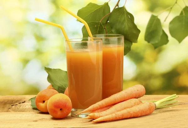 Gläser mit Karotten und Aprikosensaft auf Holztisch auf grünem Hintergrund — Stockfoto