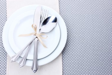 White empty plates with fork, spoon and knife tied with a ribbon on a grey tablecloth clipart