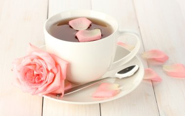 Cup of tea with rose on white wooden table clipart