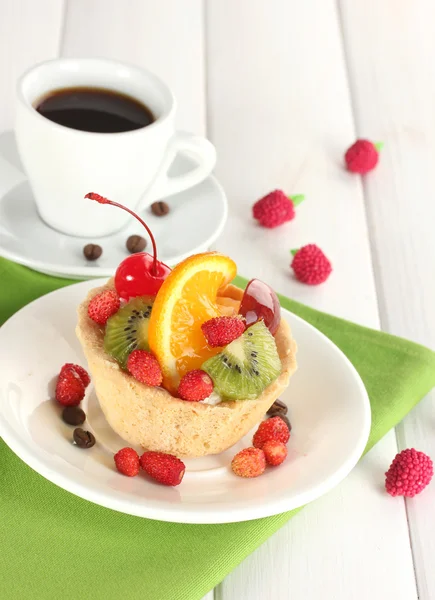 Zoete cake met vruchten op plaat en kopje koffie op houten tafel — Stockfoto