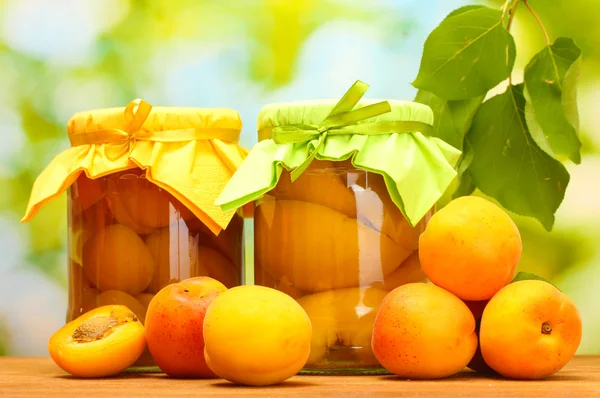 Aprikosendosen im Glas und süße Aprikosen auf Holztisch auf grünem Hintergrund — Stockfoto