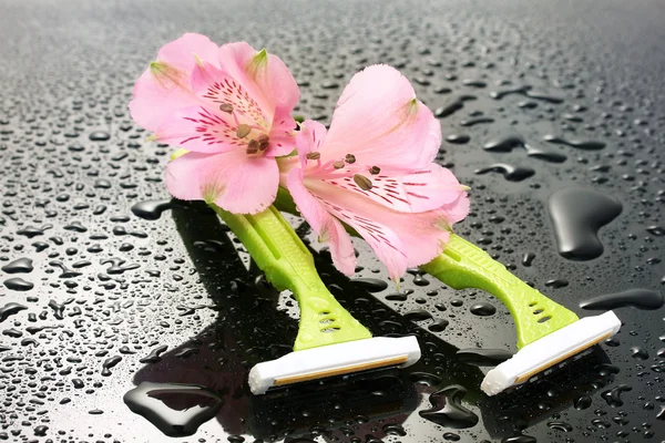 Woman safety shavers and flowers with drops on grey backgroud — Stock Photo, Image