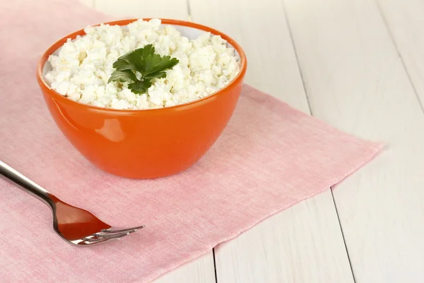 Cottage cheese with parsley in orange bowl and fork on pink napkin on white wooden table close-up — Stock Photo, Image