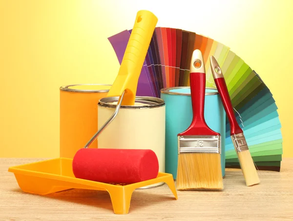 Boya, rulo, fırça ve parlak renk sarı zemin üzerine ahşap masa üzerinde paleti teneke kutular — Stok fotoğraf