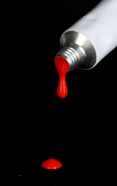 La pintura roja se desprende del tubo sobre fondo negro de cerca — Foto de Stock