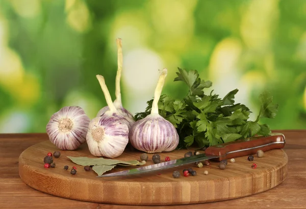Young garlic on cutting board with greenery, pepper and knife on wooden table on green background — Stock Photo, Image