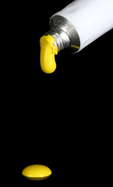 Gelbe Farbe folgt aus der Tube auf schwarzem Hintergrund in Nahaufnahme — Stockfoto